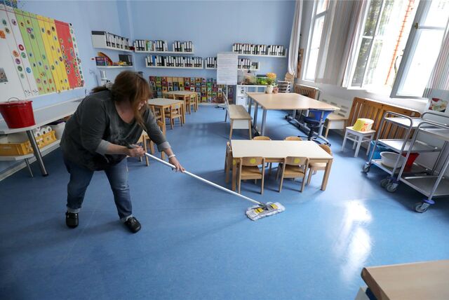 Ein Putzfrau reinigt mit dem Wischer einen Schulraum.