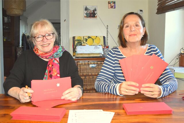 Susanne Hippenstiel und Anette Gospodarek vom Hohenheider Lädchen halten rote Umschläge in der Hand, auf denen goldene Sterne kleben.