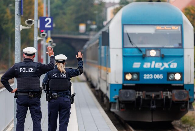 Zwei Bundespolizisten stehen am Bahnhof und winken einem Zug.
