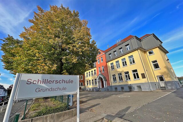Zu sehen ist das Gebäude der Schillerschule. Davor steht ein Schild mit dem Namen der Grundschule.