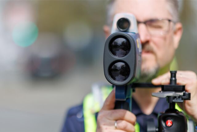 Ein Polizeibeamter kontrolliert mit einem Messgerät die Geschwindigkeit der vorbei fahrenden Fahrzeuge.