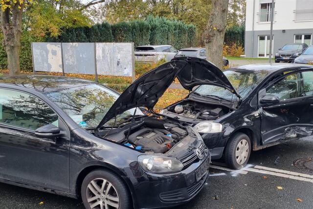 Ein schwarzes Fahrzeug ist in ein anderes schwarzes Fahrzeug gefahren. Dabei stehen beide Motorhauben offen. Ein Fahrzeug zeigt eine Schramme an der Seite.