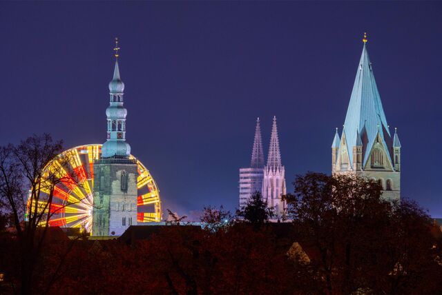 Ein leuchtendes Riesenrad ist während der Allerheiligenkirmes in Soest neben den Kirchtürmen der Stadt zu sehen.