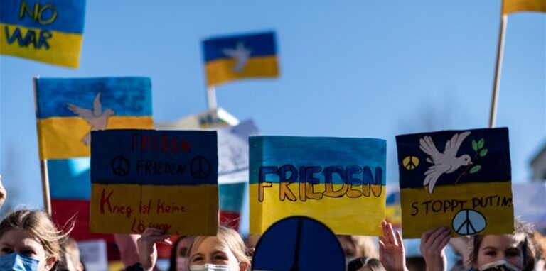 Demonstranten halten Schilder mit den Farben der ukrainischen Flagge in die Luft.