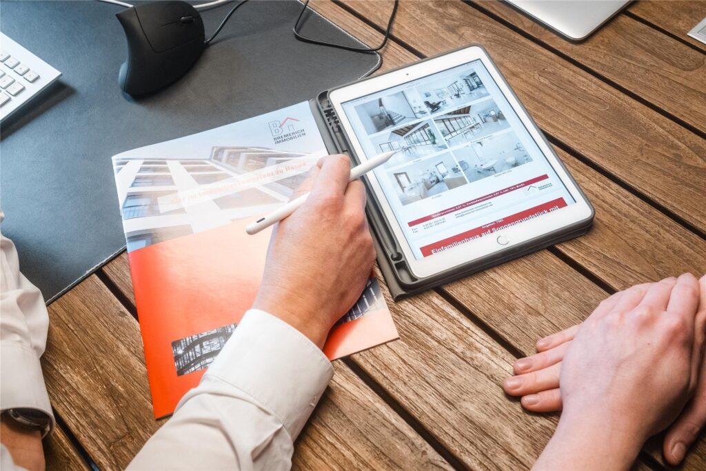 Makler von Bremerich Immobilien zeigt einem Kunden auf einem Tablet ein Haus.