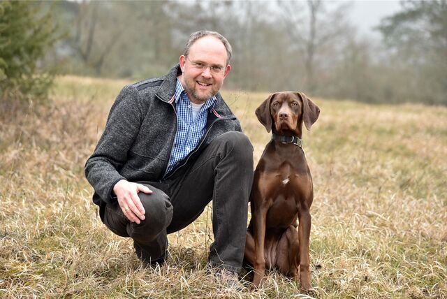 Ein Mann kniet auf einer Wiese neben einem Hund.