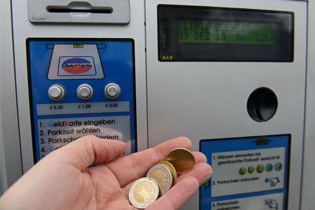 Eine Person hält Euromünzen vor einen Parkscheinautomaten