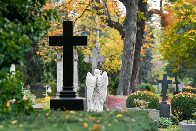 Gräber und herbstlich gefärbte Bäume auf einem Friedhof.