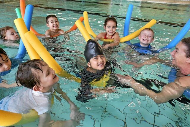 Kinder mit Schwimmnudeln planschen in einem Hallenbad