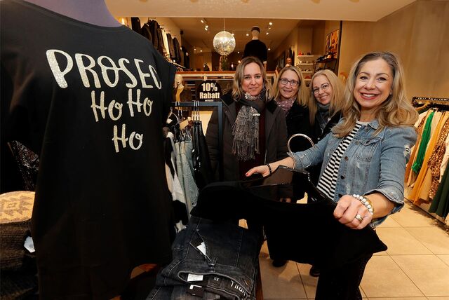 Vier Frauen stehen in einem Modegeschäft neben einer Kleiderpuppe mit einer weihnachtlichen Aufschrift.
