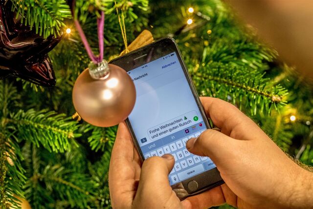 Ein Mann tippt vor einem Weihnachtsbaum eine WhatsApp-Nachricht mit Weihnachtsgrüßen.