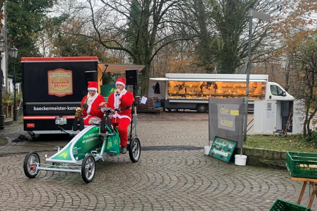 Zwei Weihnachtsmänner fahren über den Wochenmarkt am Wuckenhof in Schwerte und machen Musik. Dahinter steckt eine Aktion von Lars Wockenfuss und Stefan Käßner.
