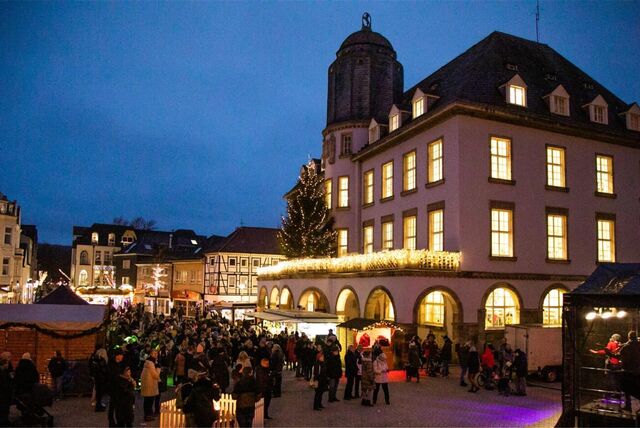 Die Mendener Innenstadt während des Mendener Winters, geschmückt mit vielen Lichtern und Büdchen. Viele Menschen sind dort unterwegs.