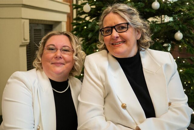 Zwei Frauen in festlicher Kleidung vor einem Weihnachtsbaum.