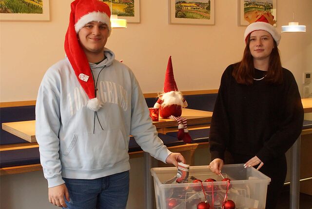 Zwei Jugendliche tragen Nikolausmützen und stehen vor einer Box voller weihnachtlicher Utensilien.