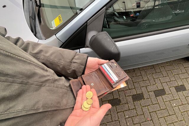 Ein Mann sucht auf einem Parkplatz Kleingeld aus seinem Portemonnaie