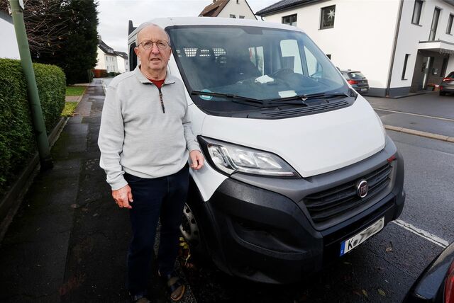 Ein älterer Mann im grauen Pullover und schwarzer Hose steht neben einem weißen Transporter. Er schaut skeptisch bis verärgert.