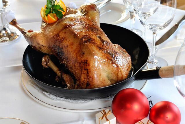 Ein Gänsebraten in der Pfanne steht auf einem weihnachtlich gedeckten Tisch.