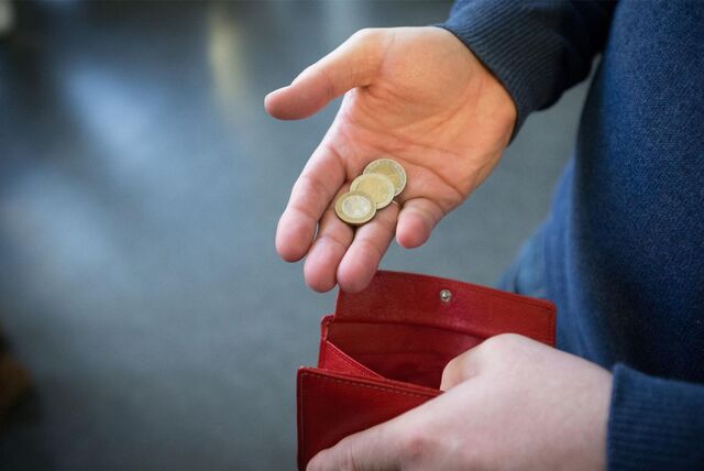 Ein Mann hält Euromünzen neben einem geöffneten Portemonnaie.