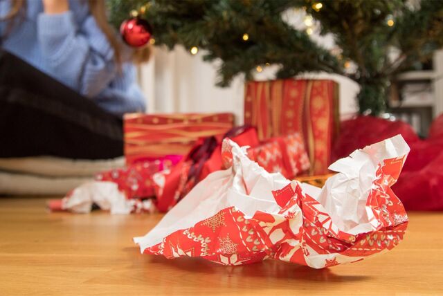 Geknülltes Geschenkpapier liegt neben verpackten Geschenken, die unter einem Weihnachtsbaum liegen.