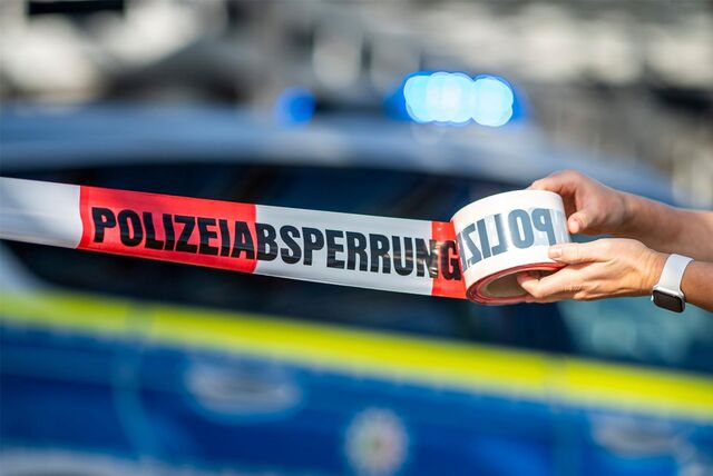 Ein Foto, was zeigt, wie eine Person ein Flatterband mit der Aufschrift „Polizeiabsperrung“ ausrollt.