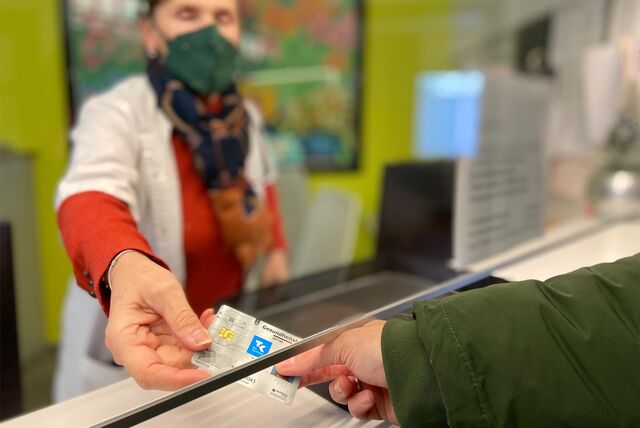 Eine Person übergibt ihre Gesundheitskarte an die Mitarbeiterin einer Apotheke.