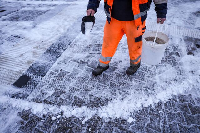 Ein Stadtmitarbeiter streut abstumpfendes Mittel auf mit Schnee bedecktem Bürgersteig.
