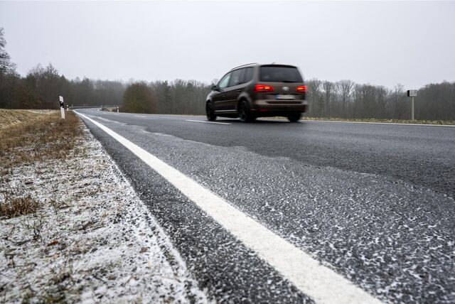 Ein Auto fährt über eine Straße, die teilweise durch Schnee und Frost glatt ist