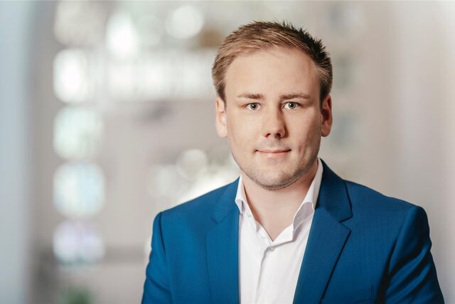 Florian Westerwalbesloh ist ein junger Mann in weißem Hemd und blauem Sakko. Er hat kurze, blonde Haare und lächelt in die Kamera.