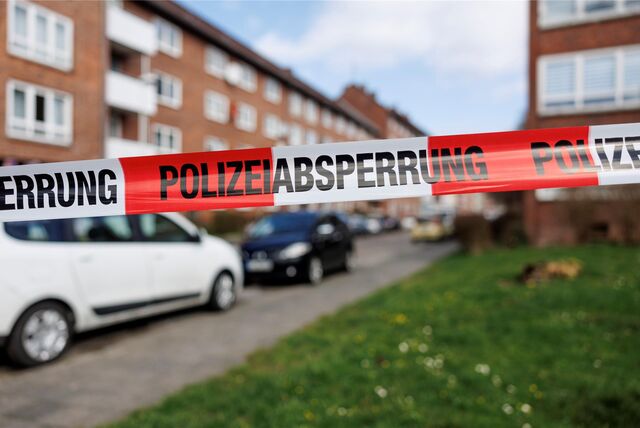 EIn Flatterband mit der Aufschrift „Polizeiabsperrung“ sperrt den Weg zu einem Wohngebiet ab.