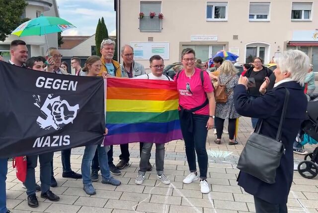 Menschen stehen im August 2023 auf dem Massener Gemeindeplatz bei einer Kundgebung. Sie tragen eine Flagge mit der Aufschrift „Gegen Nazis“ und eine Regenbogenflagge