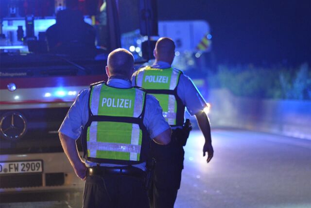 Zwei Polizeibeamte bei Nacht mit Sicherheitswesten vor einem Einsatzwagen.