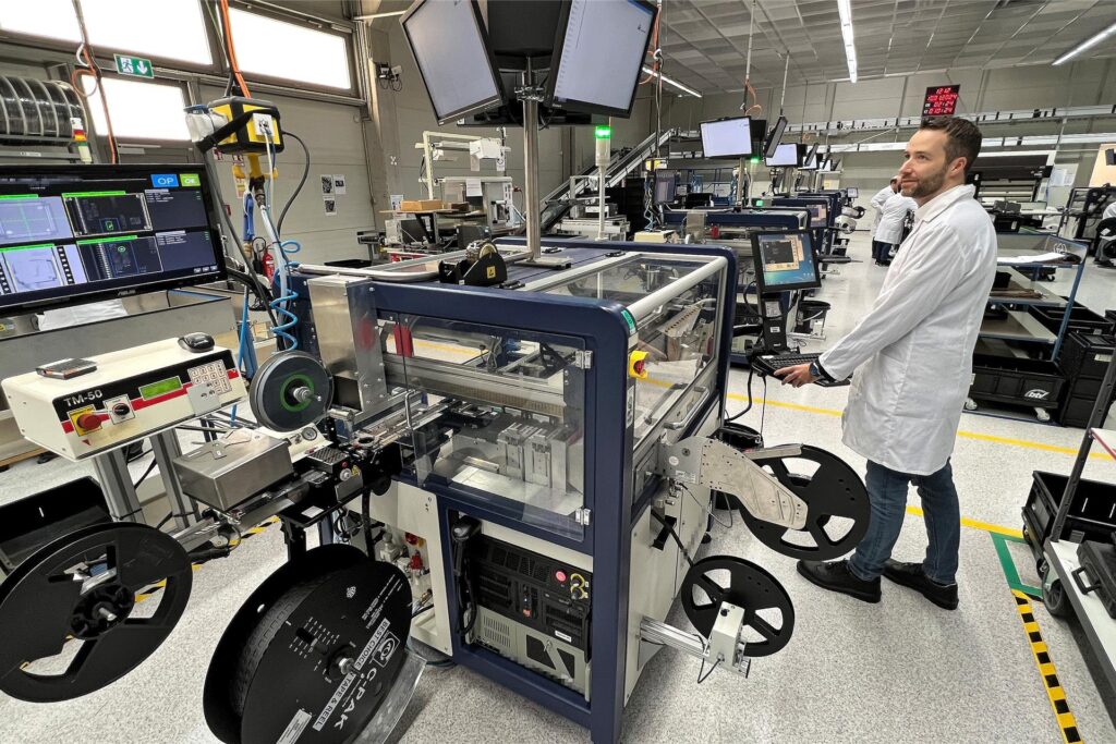 Sven Vogel ist einer der Geschäftsführer von BTV Technologies und nahm fürs Foto Platz am Bedienpult einer Programmiermaschine. Von Spulen laufen Gurte voller Chips in die Apparate, um drinnen mit Software bestückt zu werden. Sven Vogel ist einer der Geschäftsführer von BTV Technologies und nahm fürs Foto Platz am Bedienpult einer Programmiermaschine. Von Spulen laufen Gurte voller Chips in die Apparate, um drinnen mit Software bestückt zu werden.