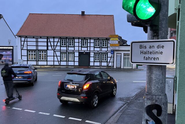 Über eine Kreuzung in Unna-Massen fahren Autos und ein E-Rollerfahrer. Am Ampelmast hängt ein Schild mit der Aufschrift „Bis an die Haltelinie fahren“.