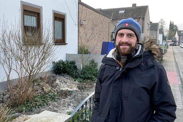 Ein Mann in Winterjacke und Mütze steht vor einem durchwühlten Vorgarten.