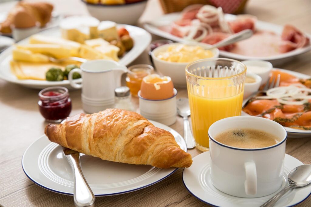 Ein üppiges Frühstück mit Croissant, Kaffee, Orangensaft und Aufschnitt steht auf einem Tisch. Ein üppiges Frühstück mit Croissant, Kaffee, Orangensaft und Aufschnitt steht auf einem Tisch.