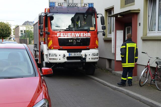 Ein Feuerwehrauto steht im Einsatz halb auf einem Gehweg. Davor steht ein Feuerwehrmann. Auf der anderen Straßenseite parken Autos.