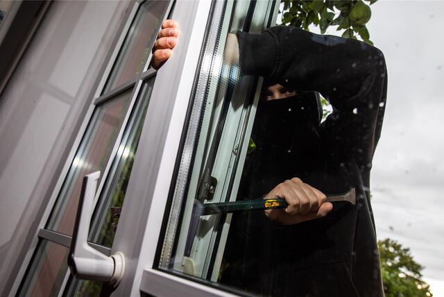 Ein Mann hebelt mit einem Brecheisen ein Fenster auf.