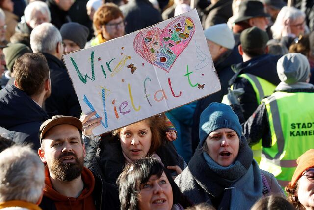 Viele Menschen sind auf dem Bild zu sehen. Eine Frau hält ein Plakat mit der bunten Aufschrift: „Wir Vielfalt“ hoch. Außerdem ist auf dem Plakat ein buntes Herz zu sehen.