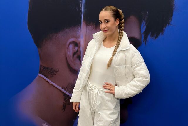 Charlotte Osigus steht vor einem Plakat, das auf das Album „Phoenix“ von twenty4tim hinweist.