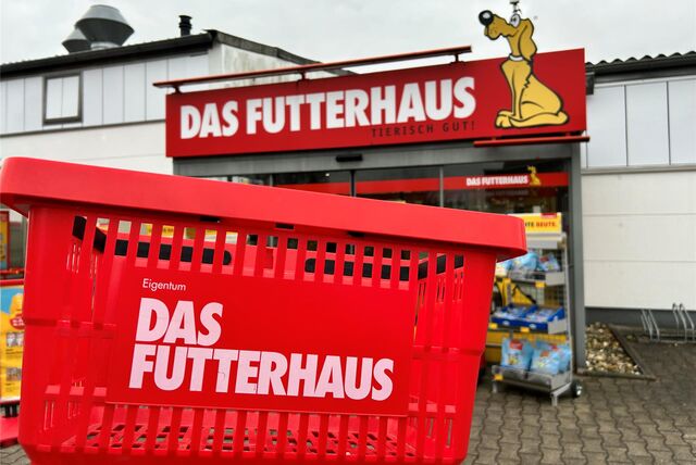 Außenaufnahme eines Tiernahrungsmittelgeschäfts. Über dem Eingang steht in weiß auf rotem Grund: Das Futterhaus. Tierisch gut! Daneben ein gelber Hund, das Symbol des Ladens. Im Vordergrund sieht man einen roten Einkaufskorb.