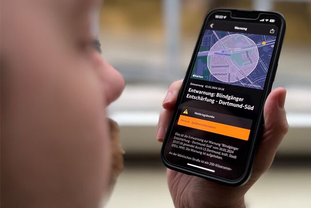 Ein Mann hält ein Smartphone mit einer Warnmeldung der Nina-App.