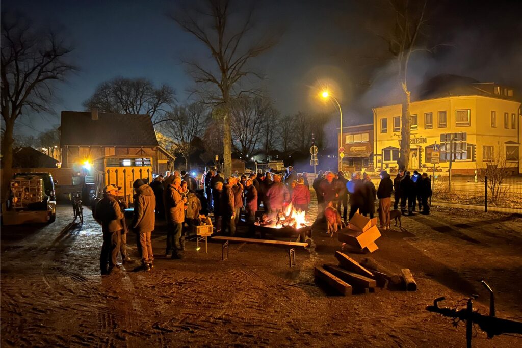 Menschen stehen draußen am Abend in der Dunkelheit um eine brennende Feuerschale.