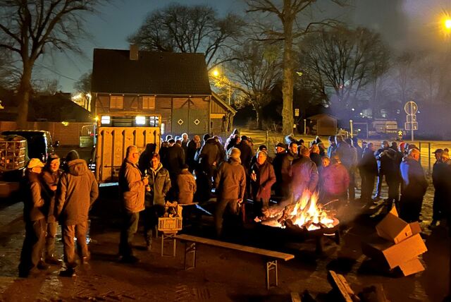 Viele Menschen stehen am Feuer unter freiem Himmel in der Dunkelheit und diskutieren