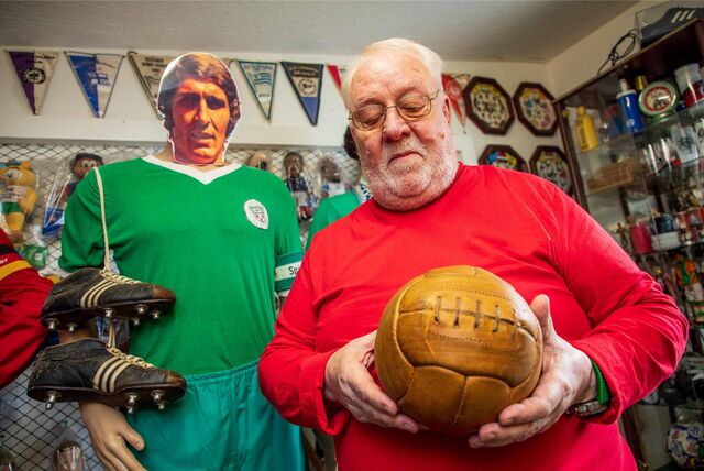 Johann Geiermann hält einen alten Fußball aus braunem Leder in Händen. Hinter ihm steht eine Schaufensterpuppe, deren Gesicht von ein Porträtfoto von Rudi Assauer verdeckt wird.