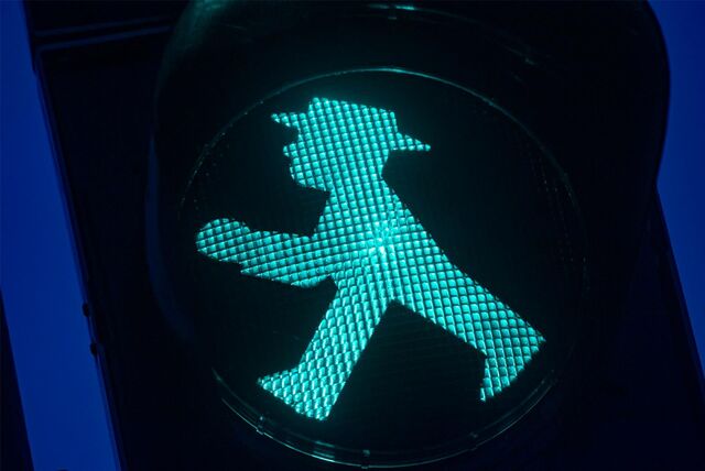 Ein grünes Ampelmännchen mit Hut läuft von rechts nach links