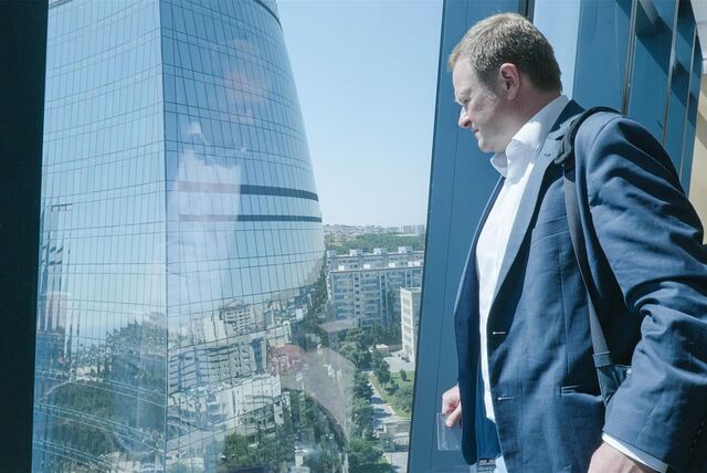 Der Bundestags- und Europaratsabgeordnete Frank Schwabe schaut aus einem Fenster auf ein Hochhaus, dessen Fenster spiegeln. Die Sonne scheint.