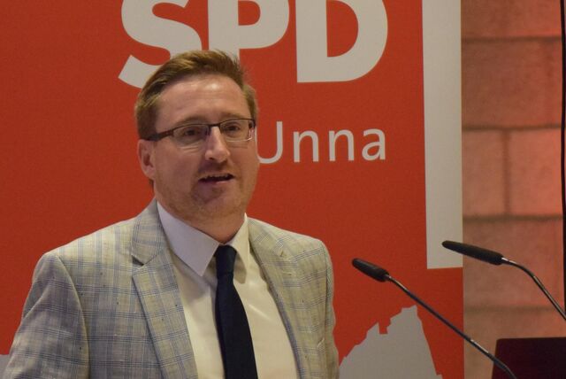 Sebastian Laaser, Fraktionsvorsitzender der SPD in Unna, spricht in ein Mikrofon. Im Hintergrund ist ein rot-weißes Banner der SPD Unna zu sehen.