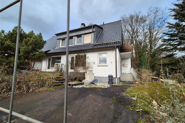 Blick durch den Bauzaun: Ein Zweifamilienhaus in Westhofen wird zwangsversteigert. Das Grundstück sieht verwahrlost aus.