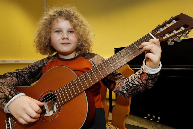 Ein Junge mit blonden Locken spielt auf einer Gitarre.